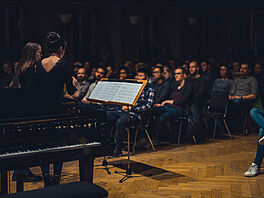 Zwei Personen auf einer ebenerdigen Bühne singen für ein Publikum.