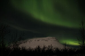 Ein nächtlicher Blick auf einen verschneiten Berg mit Nordlichtern am Himmel.