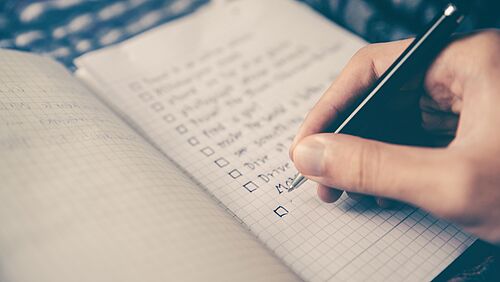 A hand writes a checklist in a notebook.