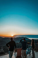 Eine Gruppe von Menschen, die einen Sonnenuntergang über einem Tal betrachten.