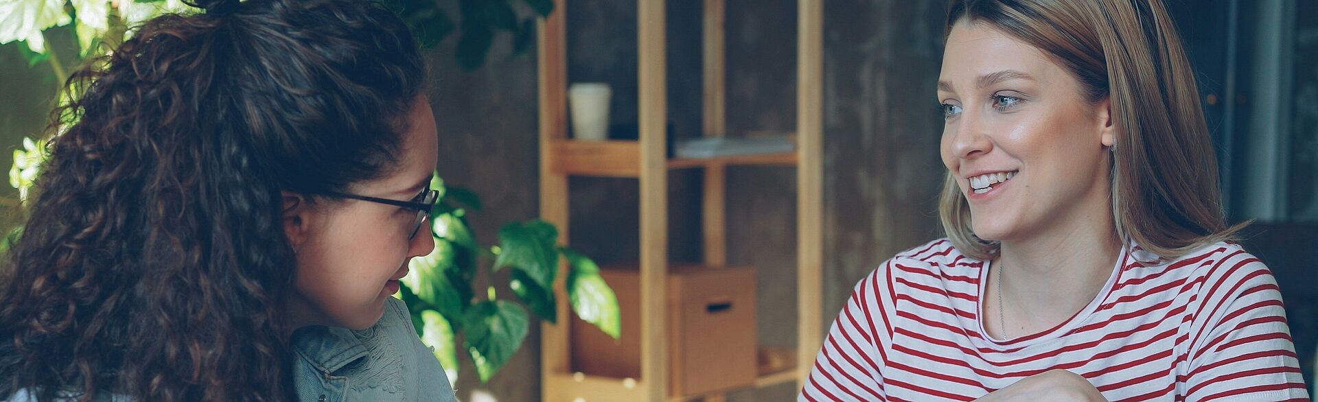 Zwei Frauen sitzen vor einem Laptop und unterhalten sich