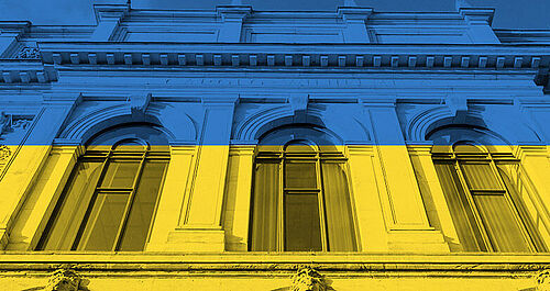Photo of the old building at TU Braunschweig in the colours blue-yellow with the lettering "We stand with Ukraine".