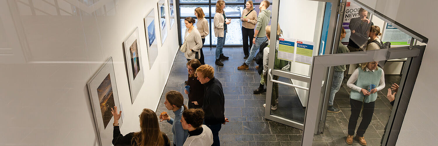 Studierende schauen sich die ausgestellten Fotos im International House an. 