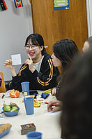 Students are sitting at a table in the seminar room playing a game. One student is smiling and holding up a piece of paper.