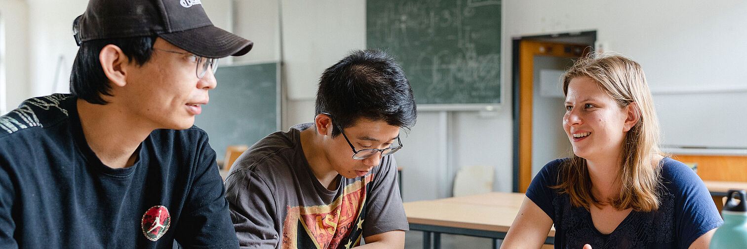 Drei Studierende sitzen an einem Tisch und lernen gemeinsam. 