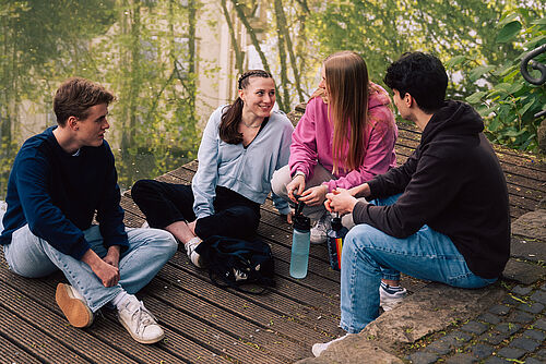 Studierende sitzen auf einem Steg an der Oker