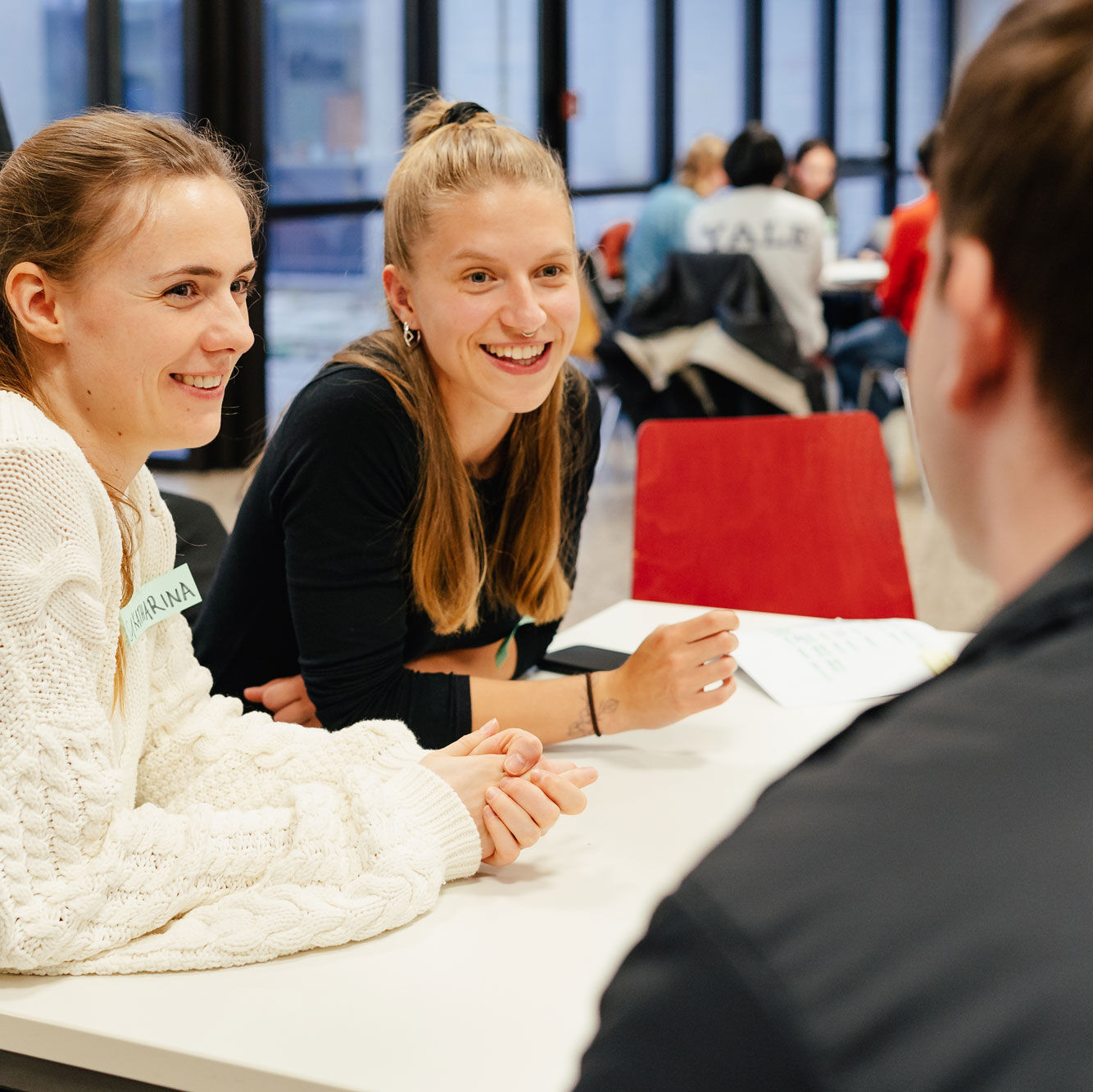 Drei Studierende sitzen an einem Tisch und unterhalten sich miteinander. 
