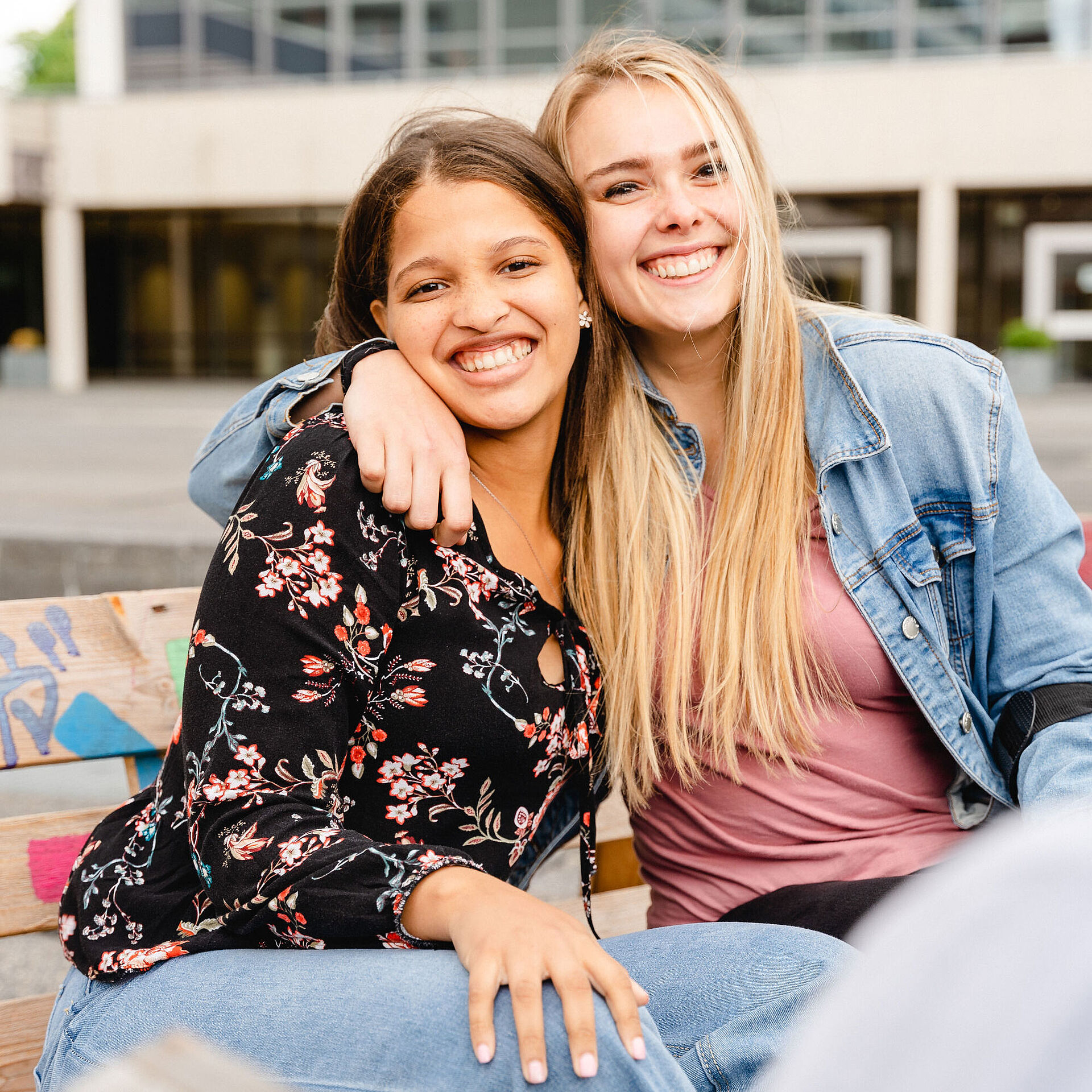 Zwei Studentinnen sitzen auf dem Universitätsplatz und umarmen sich freundschaftlich.