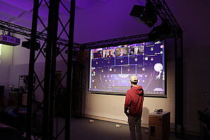 Ein Student steht vor einer Leinwand mit einer Videokonferenz