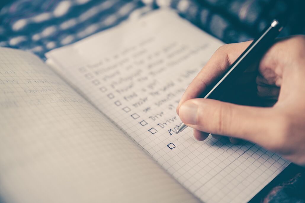 A hand writes a checklist in a notebook.