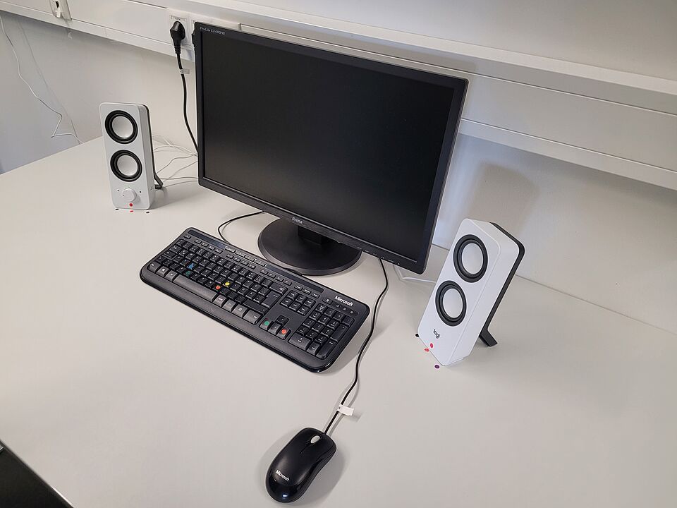 Computer monitor, keyboard, speakers, and mouse on a table.