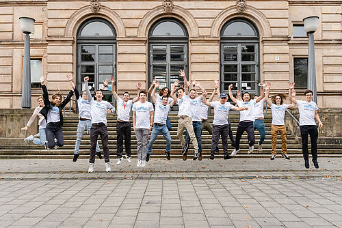 Summer School Teilnehmende springen vor dem Altgebäude