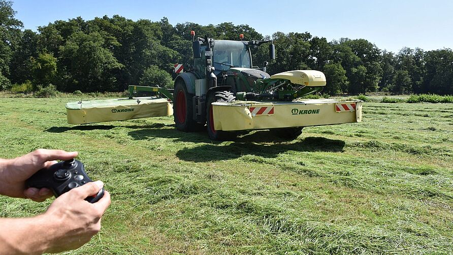 Das Symbolbild zeigt einen Traktor mit Front- und Heckmähwerk sowie einen Controller. An verschiedenen Möglichkeiten und Rahmenbedingungen der externen Steuerung als Schritt zur Automatisierung landwirtschaftlicher Maschinen und Prozesse wird im Projekt GESAL gearbeitet.