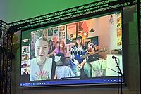 Eine Persion schaut einer Videokonferenz auf einer Leinwand zu