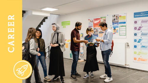 Sechs Studierende stehen im Eingangsbereich des International House und unterhalten sich in kleinen Gruppen miteinander. Auf dem Bild ist ein Banner mit der Aufschrift "Career".