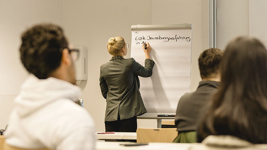Studierende sitzen in einem Workshop zum Thema Bewerben. Eine Person schreibt an ein Flipchart.
