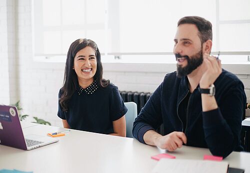 A woman and a man are sitting at a conference table with a laptop on it.