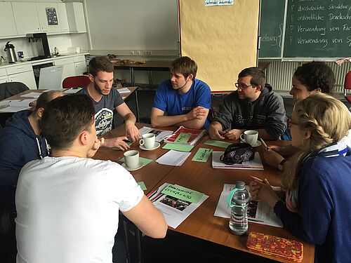 Eine Gruppe von Studierenden sitzt mit Notizen an einem großen Tisch und diskutiert.
