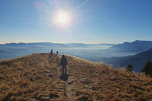 Eine kleine Gruppe von Menschen steht auf einer Klippe und überblickt ein weites Tal, das von großen Bergen umgeben ist.