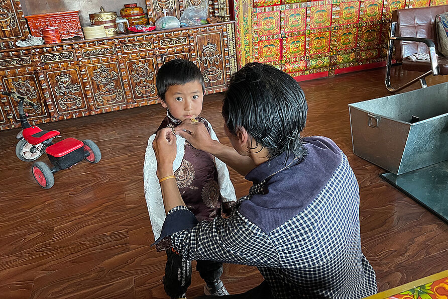 Tashi zieht seinem Sohn tibetische Kleidung an.