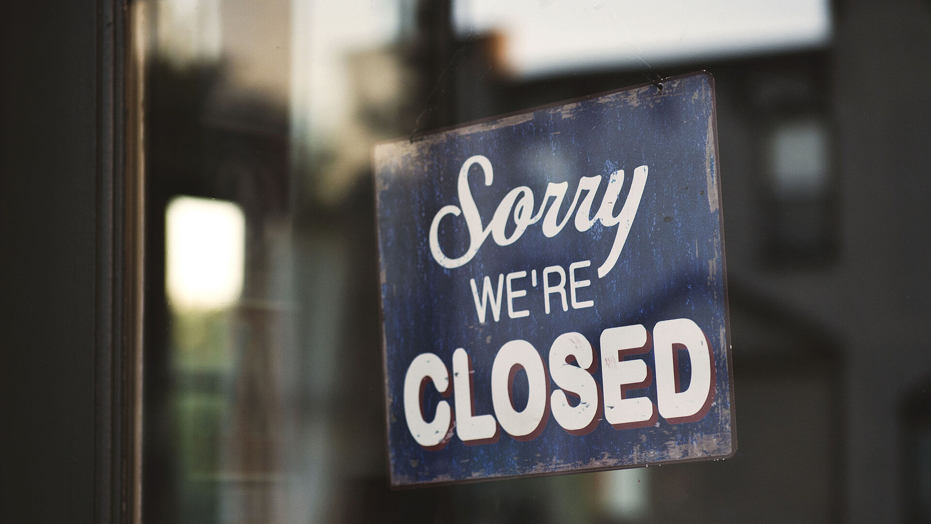 Closeup shot of a sign that says "Sorry We're Closed" hanging on a glass door