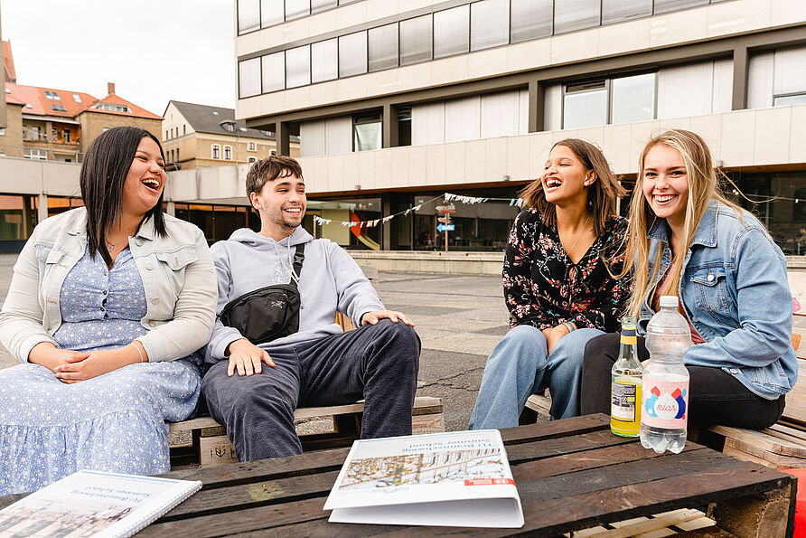 Vier Studierende sitzen auf dem Universitätsplatz und lachen gemeinsam.