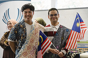 Two members of the Malaysian Braunschweig Association are standing at a bar table and smiling at the camera.