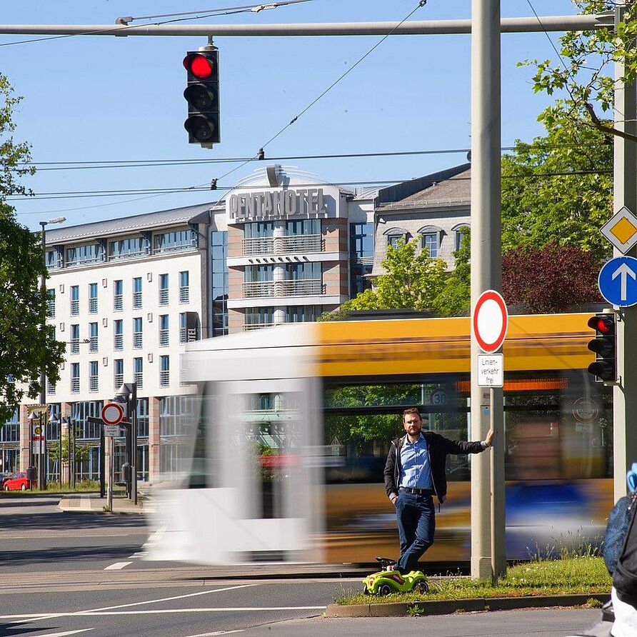 Person an einer Straßenkreuzung in Braunschweig. Im Hintergrund eine Straßenbahn.