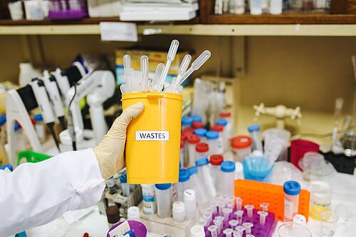 Wissenschaftler, der Laborabfälle in einer kontrollierten Umgebung handhabt, mit Fokus auf Sicherheit und Sauberkeit.