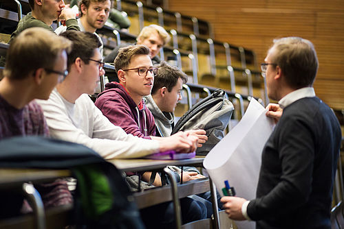 Studierende reden in einem Hörsaal mit einem Dozenten