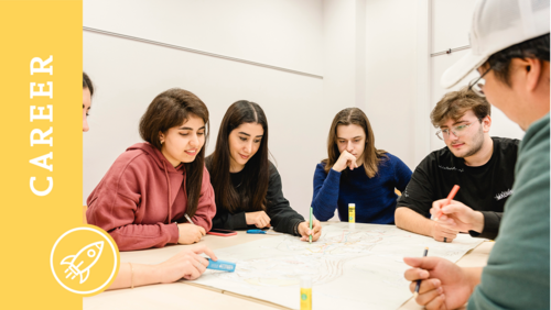 Mehrere Studierende sitzen an einem Tisch in einem Seminarraum und bearbeiten eine Gruppenarbeit. Auf dem Bild ist ein Banner mit der Aufschrift "Career".