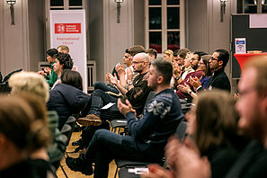 Conference participants sit in the auditorium of the Haus der Wissenschaft and applaud.