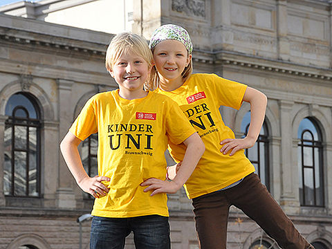 Zwei Kinder tragen gelbe T-Shirts mit dem Logo der Kinder-Uni.