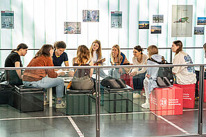 Eine Gruppe Menschen sitzt auf Sitzwürfeln in einem modernen Raum. Alle hören gespannt einer Person zu.