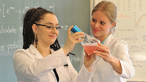 Zwei Studentinnen betrachten einen Erlenmeyerkolben am Institut für Mikrobiologie