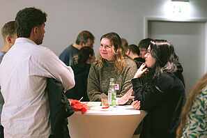 Conference participants stand together at a bar table and chat.