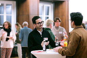 Two conference participants stand together at a bar table and chat.