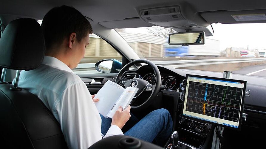 Mitarbeiter in einem Fahrzeug auf der Autobahn beim Lesen. Das Auto fährt vollständig eigenständig.