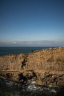 Ein Angler sitzt an auf einr Klippe am Meer in Spanien.