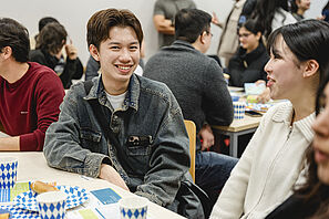 Students sit at tables decorated in Bavarian style in the seminar room. One person laughs at the camera.