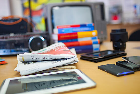 Symbolfoto: Zeitung, Bücher, Kamera, Smartphones und Tablet auf einem Schreibtisch