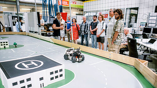 CampusXperience im NFF-Technikum: Wissenschaftlicher Mitarbeiter des ITL erläutert autonome Roboterfahrzeuge einer Besuchergruppe
