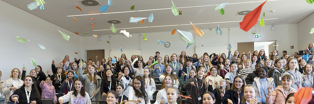 Kinder werfen ihre selbstgebastelten Papierflieger im NFF-Hörsaal im Rahmen des Zukunftstages 2025. 