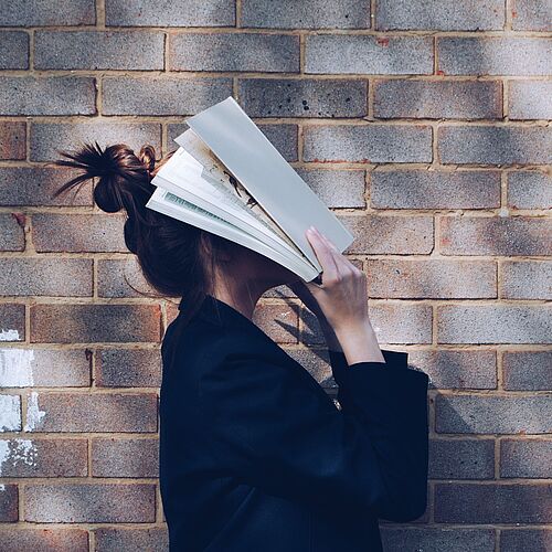 Eine Frau versteckt resigniert ihr Gesicht hinter einem Buch.