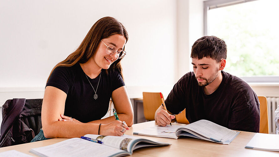 Zwei Studierende sitzen an einem Tisch und lernen.