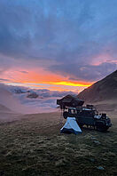 Ein Blick auf den Sonnenuntergang in den Bergen mit einem Auto mit Dachzelt und Campingzelten im Vordergrund.
