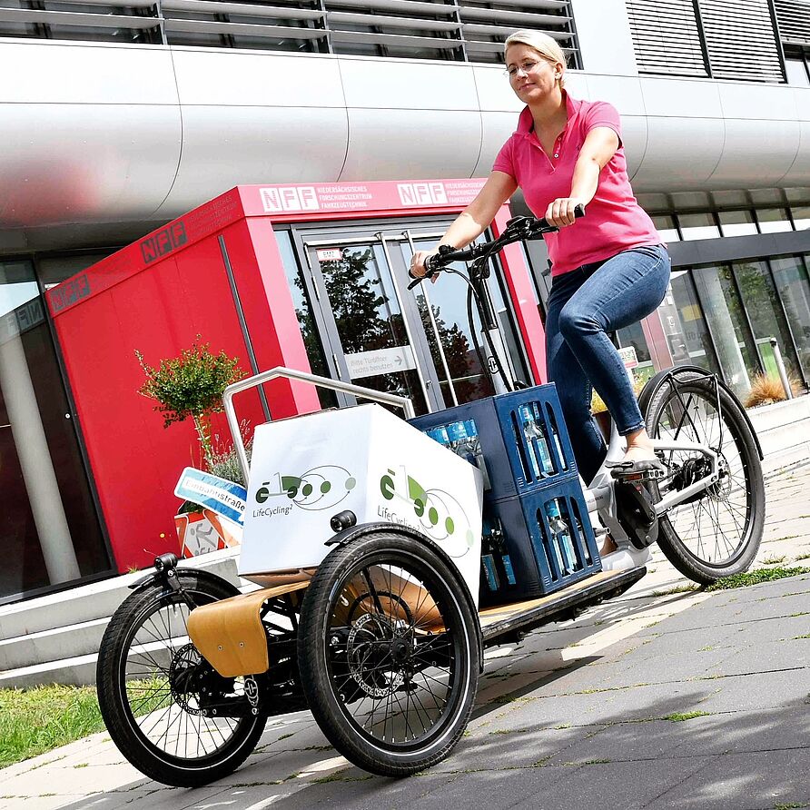 NFF-Mitarbeiterin auf einem Lastenfahrrad vor dem NFF-Gebäude.