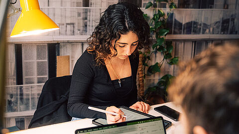 Studierende arbeitet an einem Lernplatz der TU am Tablet. Ihr Gegenüber (im Bild nur angeschnitten sichtbar) arbeitet am Laptop. 