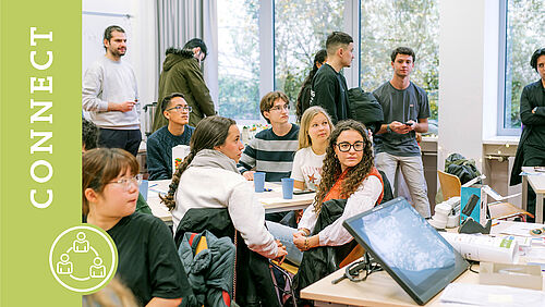 Mehrere Studierende sitzen und stehen in einem Seminarraum im International House.