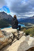 Eine Studentin sitzt auf einer Klippe in den Rocky Mountains mit Blick in die kanadische Berglandschaft. 